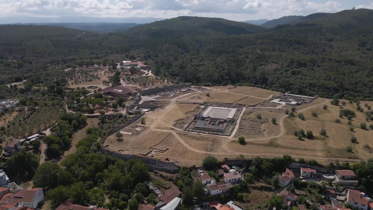 Rastreamento aéreo suave sobre Conímbriga, revelando o layout de estruturas romanas, pátios e caminhos de conexão. Uma imagem de drone elevada captura a beleza e a complexidade das ruínas antigas de Conímbriga.