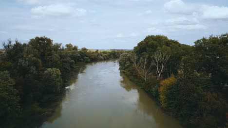 drone shot of muddy slow river between fields and trees
