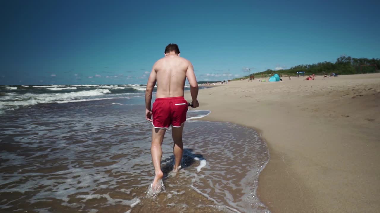 joven en shorts rojos camina en una playa junto al mar-1