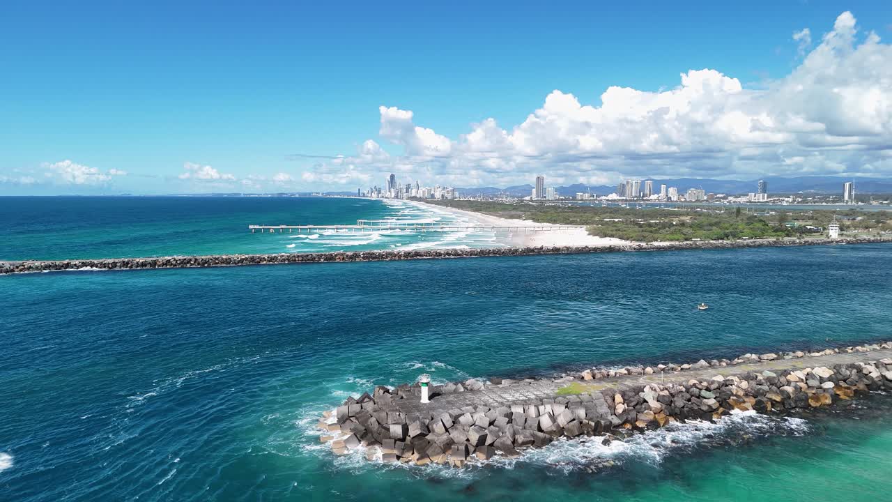 Aerial view of a man made seaway inlet with rock break walls and sand pumping pipe structure close to a towering city skyline. Gold Coast Australia