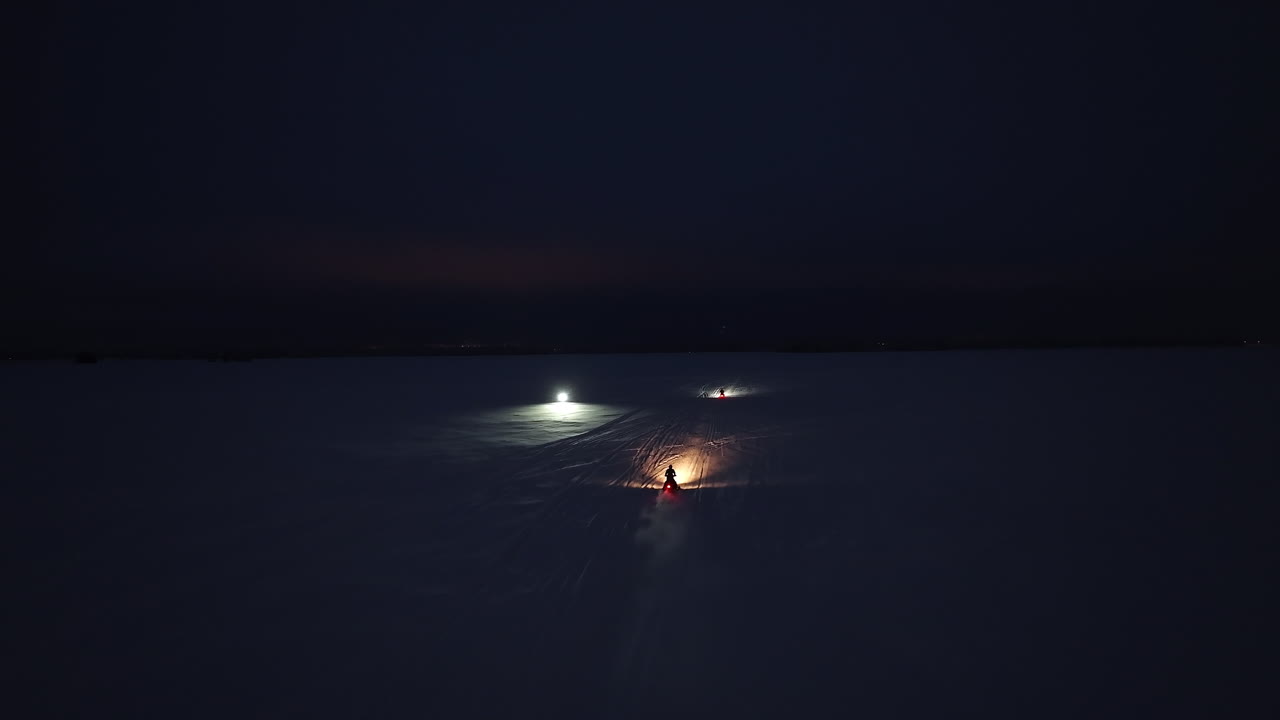 Aerial view of snowmobiles driving on a frozen lake, winter night in Lapland