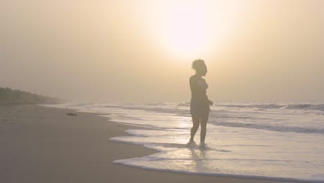 Young woman walks on the seashore during sunset