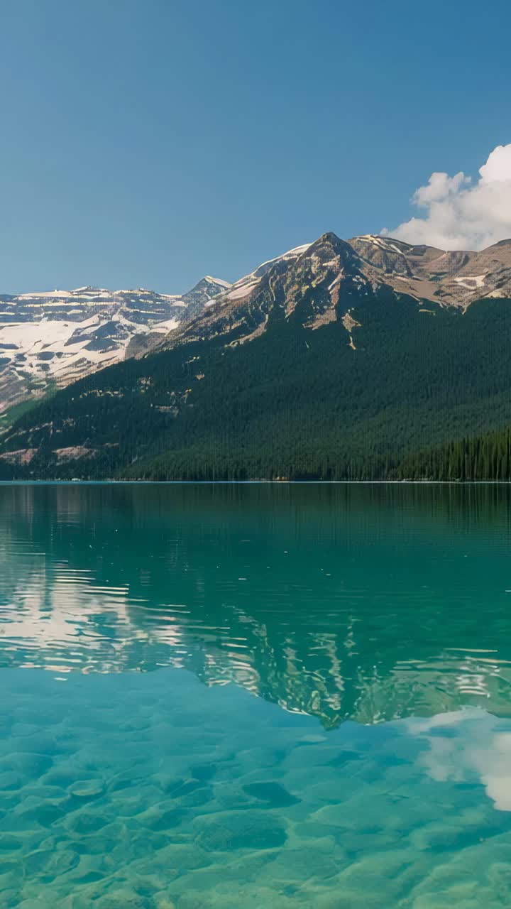 Vertical video: Camera tilting, framing turquoise lake with stones and snowy mountain in valley