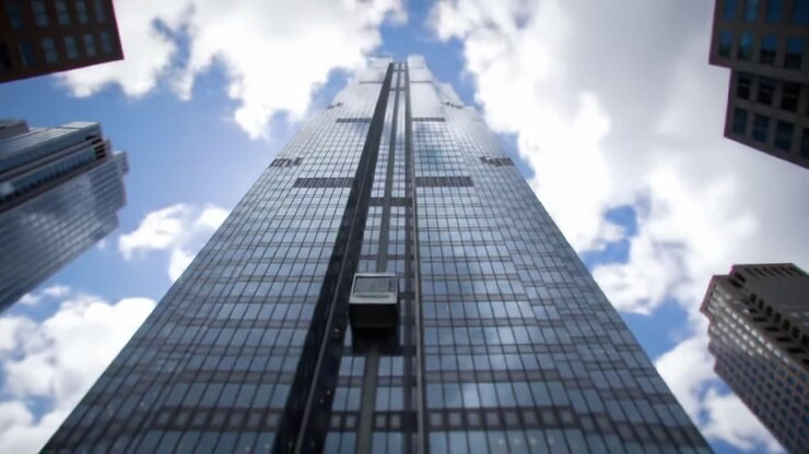Una vista impresionante de un imponente rascacielos contra un cielo azul brillante, capturada desde el nivel del suelo, mostrando su arquitectura majestuosa y características de diseño moderno.