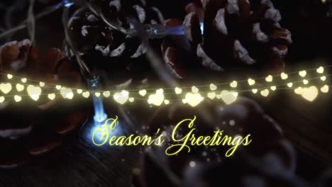Animation-of-text,-season's-greetings,-in-yellow,-over-string-lights-and-pine-cone-decorations