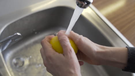 top close shot as opening the tap, then hands washing a yellow lemon with water in the kitchen