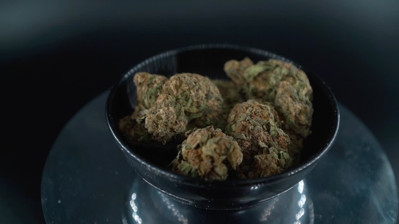 Grayish Green Dried Marijuana Buds Close Up Shot, pile of dried marijuana plants in a shiny bowl, trichomes strains, on a reflecting rotating stand, studio lights, cinematic zoom out slow motion
