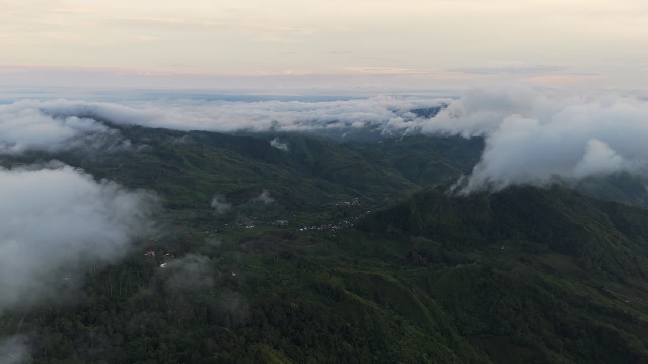 Moody 4K aerial drone footage flying over lush green mountain peaks covered in thick fog. Atmospheric landscape with low clouds rolling through the deep valleys