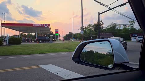 stock video of a white suv turning onto a road at sunset near a circle k gas station. captures a calm suburban moment with vehicles, power lines, and a colorful sky in the background.