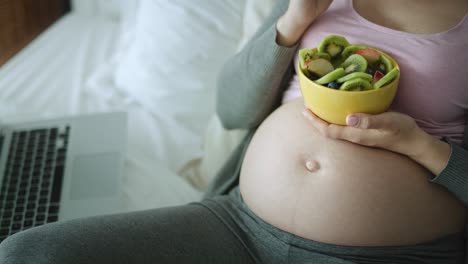 video of pregnant woman eating a bowl of fresh fruits.