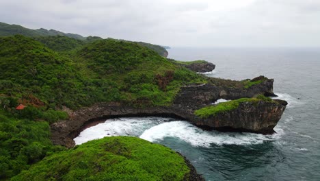 aerial dolly in towards coastal rocky cliffs with rainforest and crashing waves