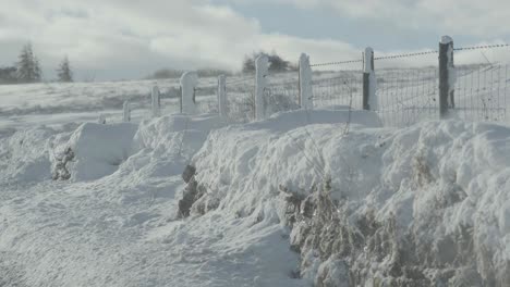 Looking-past-a-wire-fence,-on-a-country-road-across-a-snowy-field