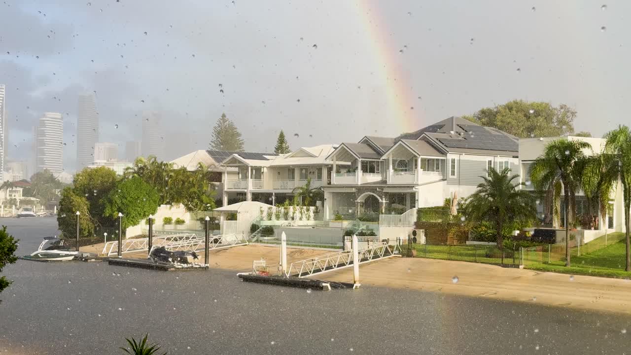 Luxury homes by a canal under a sunshower with a vibrant rainbow in Gold Coast, Australia
