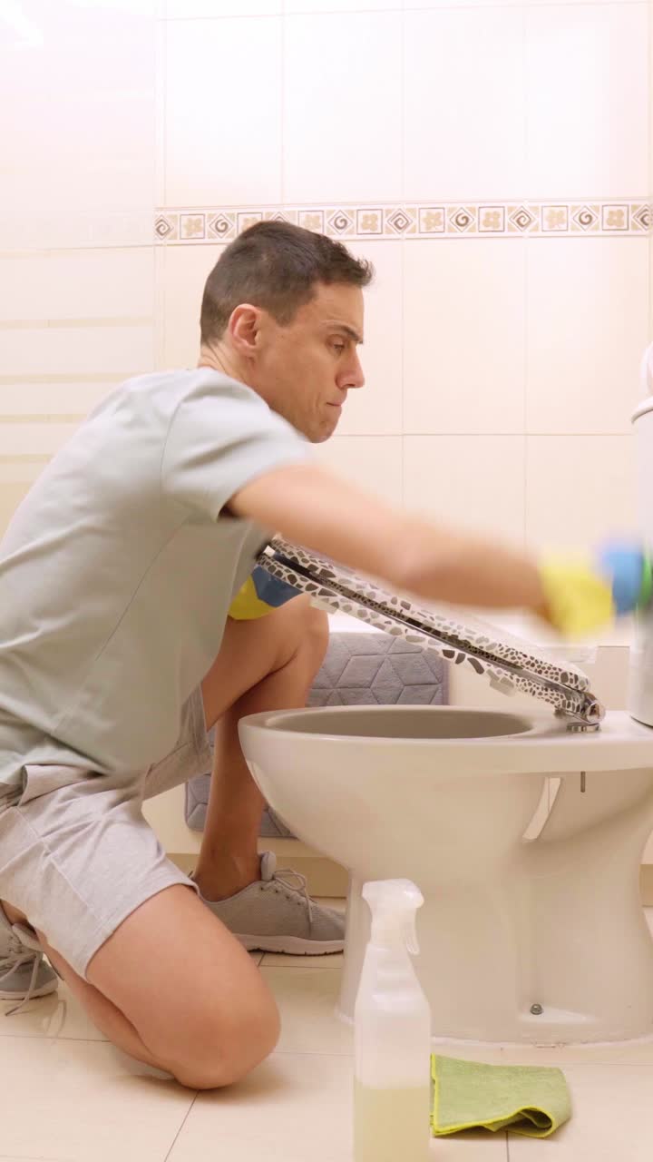 Man cleaning toilet in bathroom with disinfectant and sponge