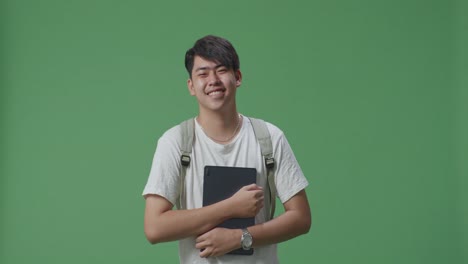 un estudiante asiático sonriente sosteniendo una tableta y caminando en el estudio de pantalla verde