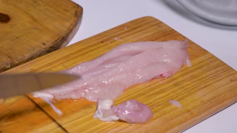 Hands-of-man-cut-breast-into-squares-on-wooden-cutting-board-and-put-on-glass-pot