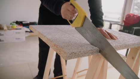 medium shot of a male handyman using a handsaw to cut an acoustic panel for the ceiling house renovation diy