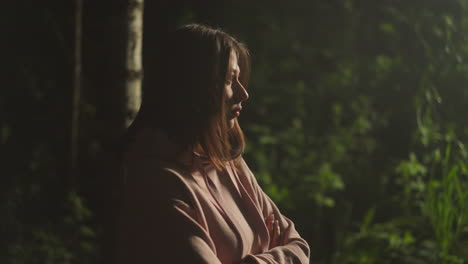 pensive young woman breathes heavily in fresh forest air while standing under light of street lamp. lonely female person in warm coat feels sad while relaxing in nature