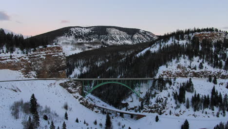 avión no tripulado cinematográfico vail avon acantilado rojo icónico puente de colorado mitad del invierno coches conduciendo en la nieve al atardecer pan movimiento hacia adelante