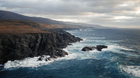 rocky ocean coast with black rocks and waves smashing on cloudy day, summertime holiday