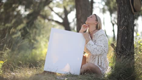 happy woman artist in apron dancing holding canvas with her painting in her hands in studio