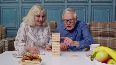 una pareja de ancianos, abuelo y abuela, descansando en el sofá, jugando a un juego con bloques de madera en casa.