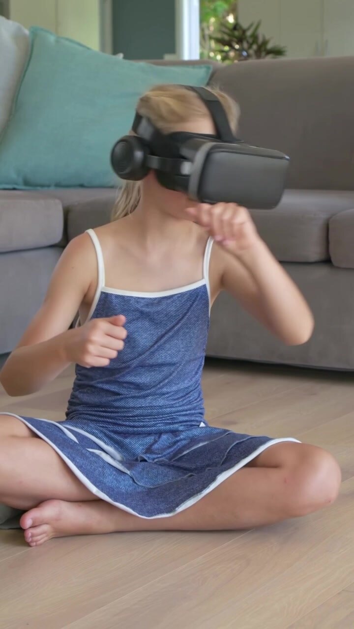 Video verticale: Ragazza in abito blu con visore VR, che tocca e scorre con le mani, a casa.