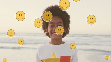 Animation-of-emoji-icons-over-happy-african-american-boy-on-sunny-beach