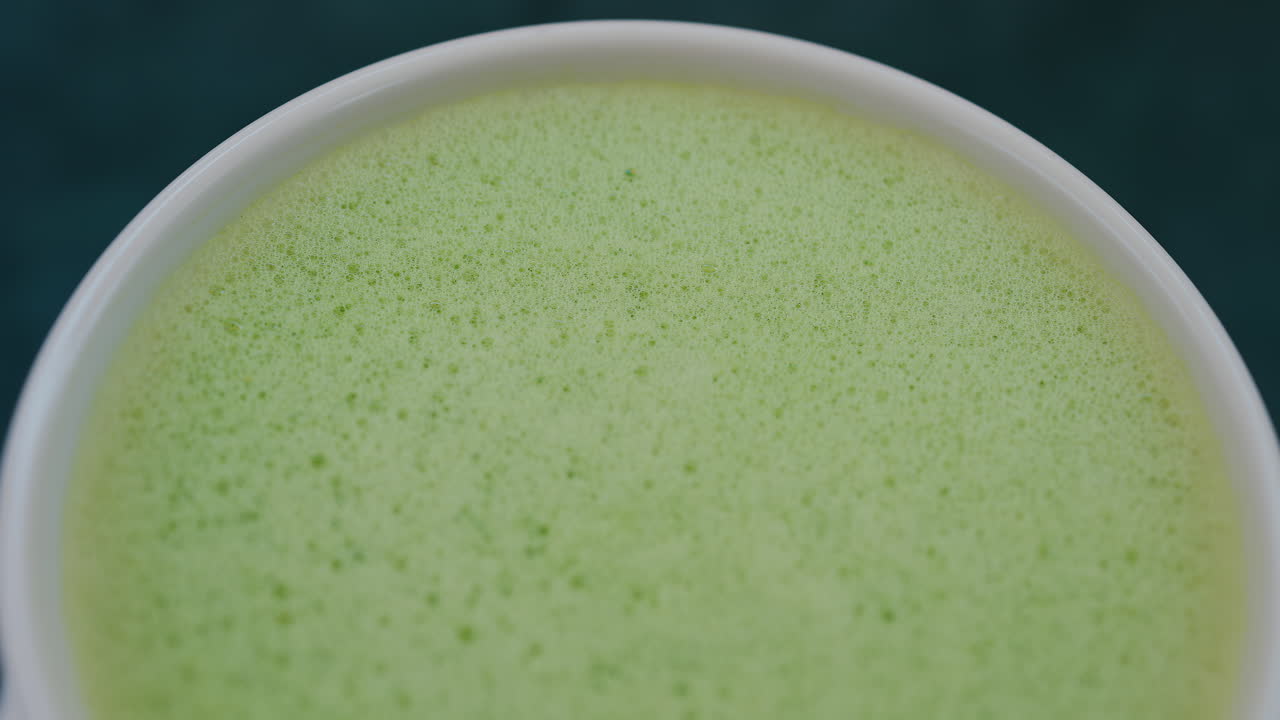 Close up of a smooth matcha latte with vibrant green foam in a white cup