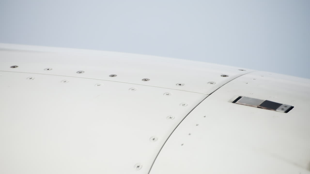 A close-up of an airplane wing, highlighting the mechanical features and smooth texture while in flight. The view emphasizes the engineering and design of the structure