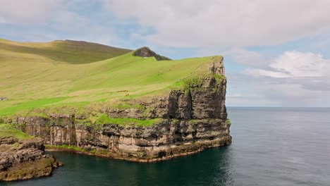 un impresionante acantilado costero con hierba verde, cielo azul y océano cerca de gjógv, faroe