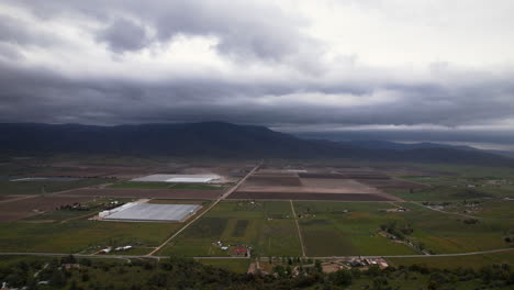 Aerial-view-of-Tehachapi,-California-on-a-cloudy-day-with-large-farm-fields,-greenhouses,-and-mountains-in-the-background