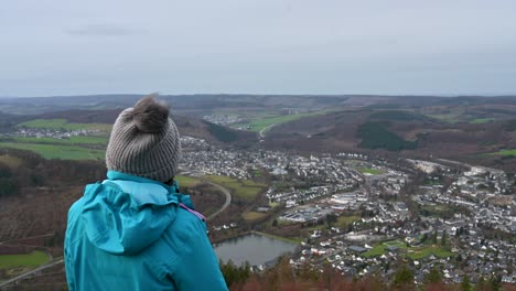 ganando la vista de sauerland: una mujer de mediana edad con una chaqueta azul y una cabeza gris cálida disfrutando de la vista de olsberg después de una larga caminata en un día nublado