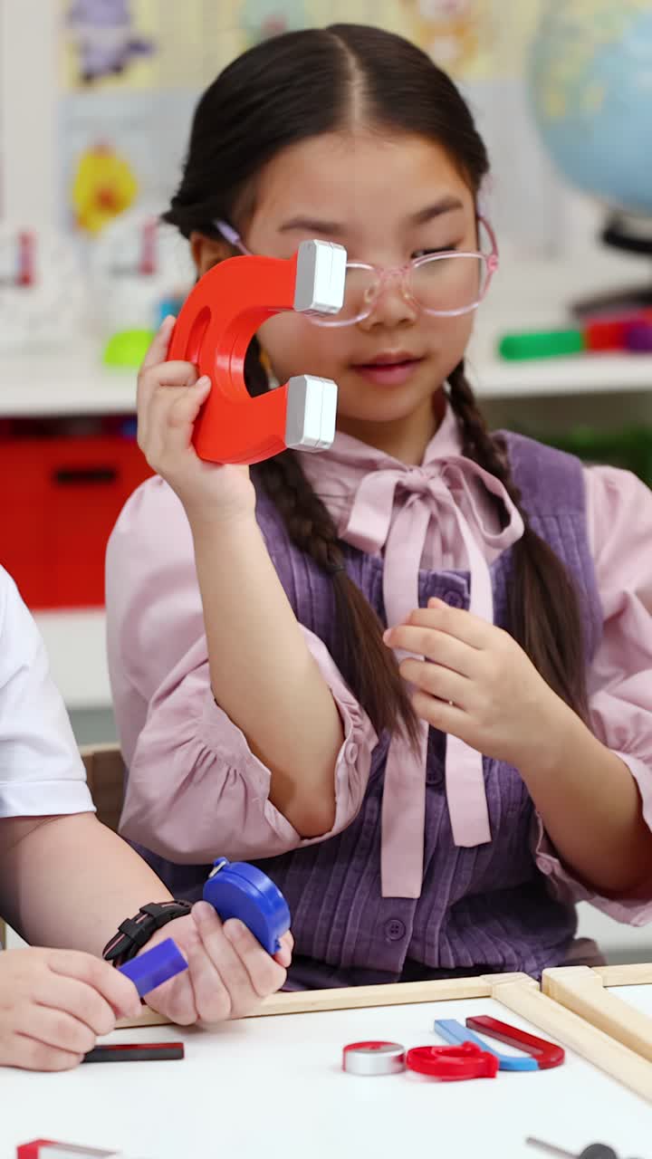 Seorang gadis muda menjelajahi gaya tarik magnet menggunakan magnet tapal kuda selama pelajaran sains di kelas.