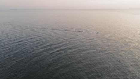 a boat motors along a calm sea during a winter sunrise off the coast of maine aerial