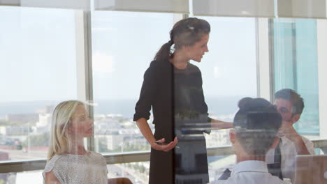 Businesswoman-Leads-Meeting-Around-Table-Shot-Through-Door