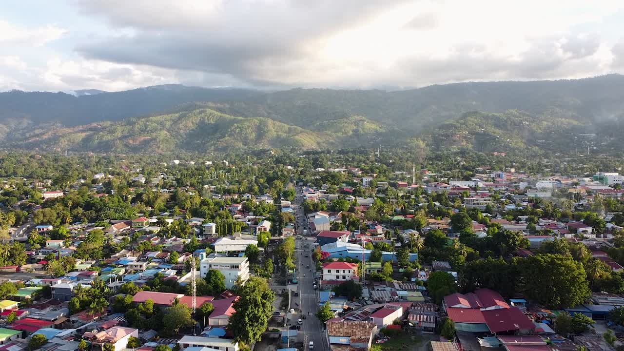 Panoramic aerial view of capital city Dili, Timor-Leste, with houses, buildings, green trees, and rugged mountains in distance