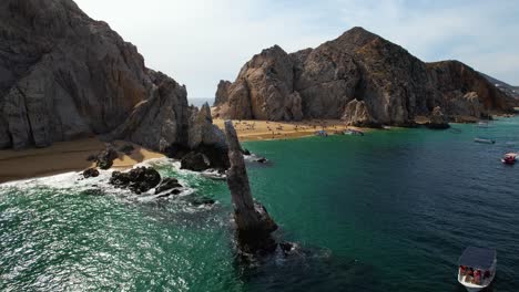 Aerial-view-around-rock-formations-while-tourists-ride-boats-in-Cabo-San-Lucas,-Mexico---orbit,-drone-shot