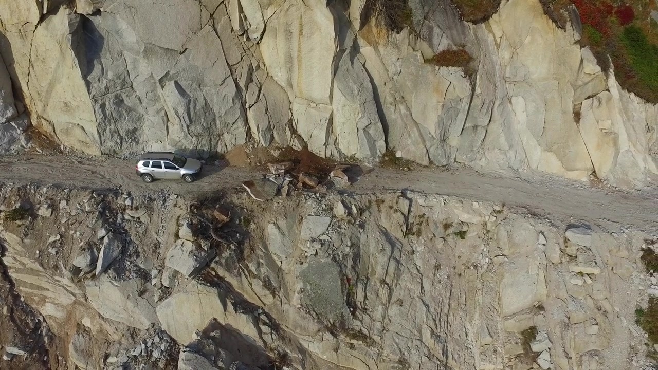 SUV argentato che percorre una stretta strada di montagna a strapiombo