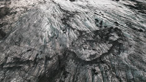 aerial tracking view looking down on iceland glacier covered in volcanic sediment