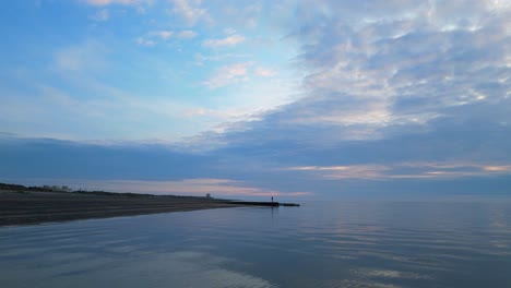 Figura-Distante-Caminando-Sobre-El-Embarcadero-Con-Vuelo-Bajo-Sobre-El-Mar-Suave-Al-Atardecer-En-La-Playa-De-Fleetwood,-Lancashire,-Reino-Unido