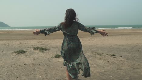 Woman-on-her-back-walking-on-the-shore-of-a-beach-while-the-wind-moves-her-dress