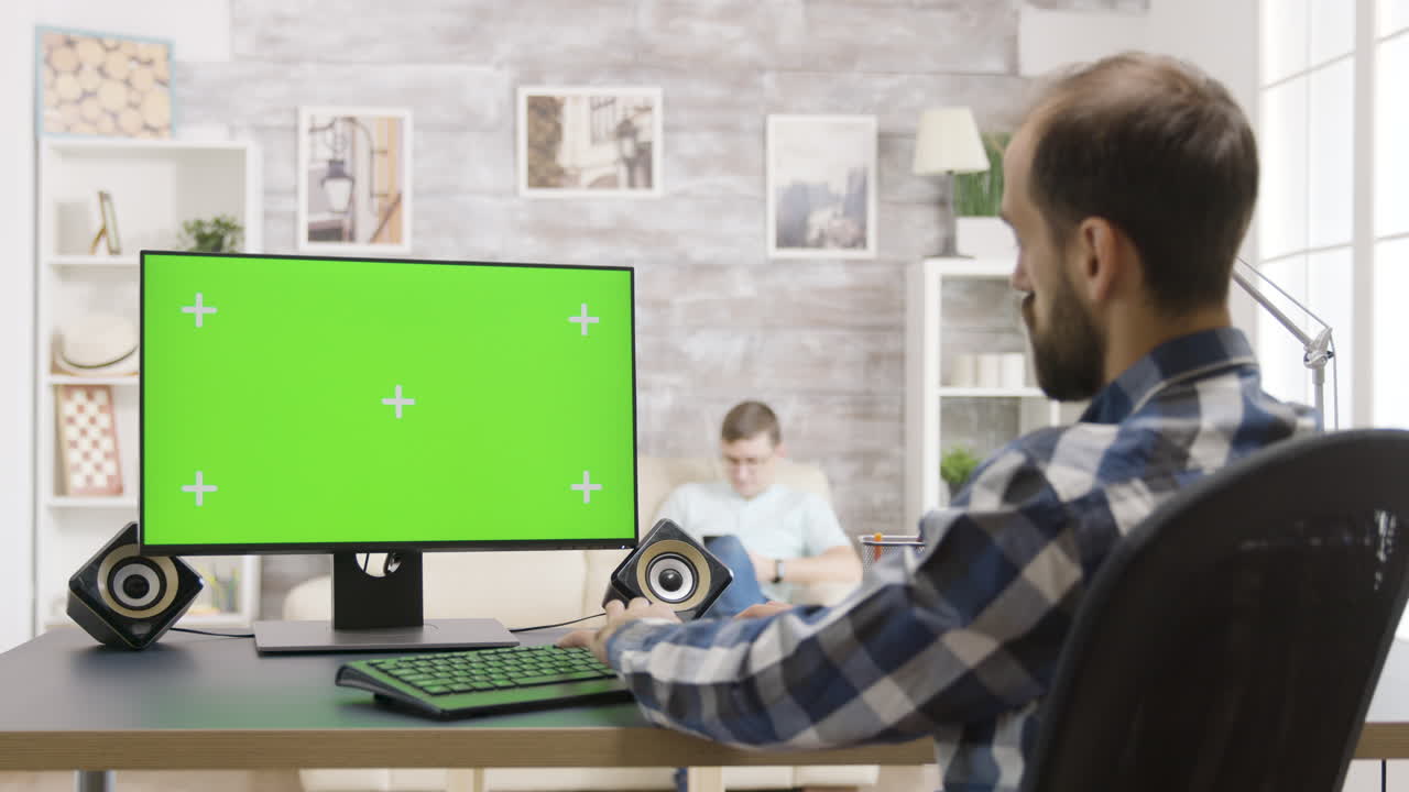 Man working on a computer with green screen at home