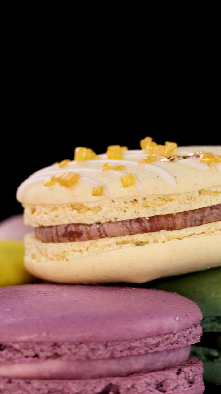 Çeşitli pastel makaronlar, parlak stüdyo ışığı altında sorunsuz bir şekilde dönerek, parlak siyah yansıtıcı bir yüzey üzerinde dokuları ve canlı renkleri vurguluyor.
