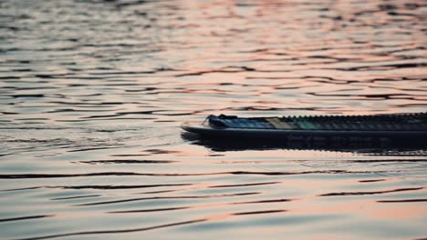 Beine-Eines-Mannes,-Der-Auf-Dem-Paddelbrett-Steht,-Paddelbrett-Am-See-Der-Nationen-Mit-Sonnenuntergangsreflexionen-Auf-Dem-Wasser-In-Sherbrooke,-Quebec,-Kanada