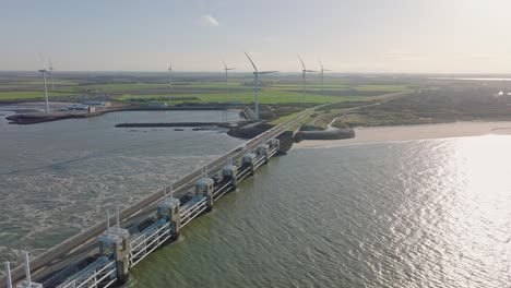 aerial slow motion shot of the open eastern scheldt storm surge barrier, wind turbines and farmland on a beautiful sunny day around sunset