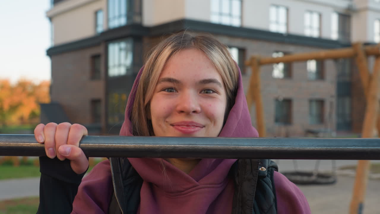 Portrait of energetic female trainer making playful facial expression while gripping horizontal pull up bar during outdoor workout session in urban park, showcasing strength, joy, and fitness
