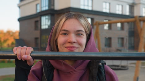 portrait of energetic female trainer making playful facial expression while gripping horizontal pull up bar during outdoor workout session in urban park, showcasing strength, joy, and fitness