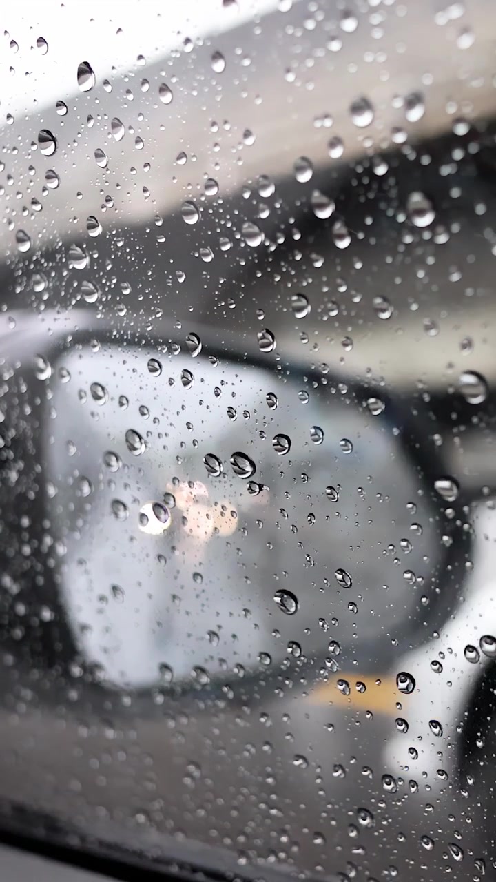Raindrops on side window, blurred traffic reflections, overcast daylight, stationary camera, urban roadside