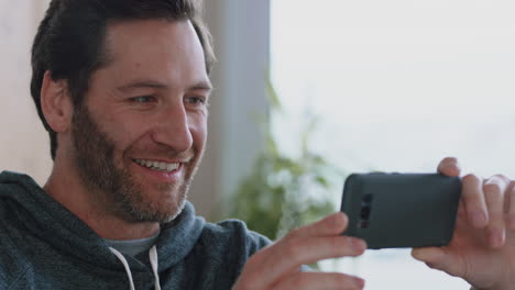 happy young man using smartphone browsing online watching entertainment enjoying mobile phone communication relaxing at home